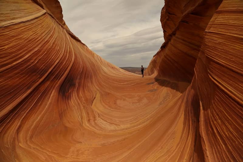 A person stands in a sandstone canyon with wavy formations.