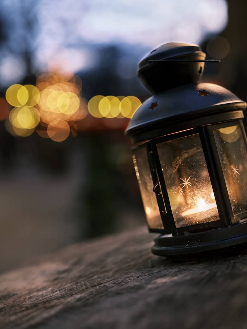 A lit lantern sits on a wooden surface outdoors.