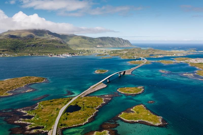 Scenic bridge connecting islands over clear blue water with mountains.