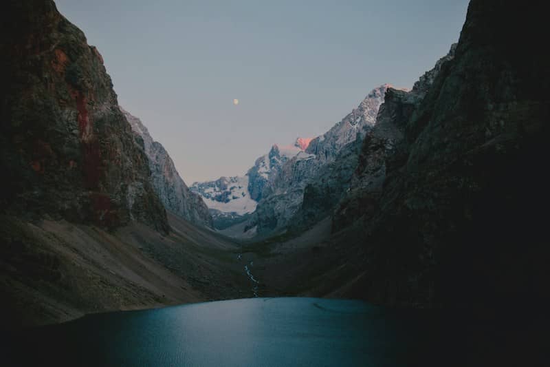 A small lake nestled between steep rocky mountains under a pale moon