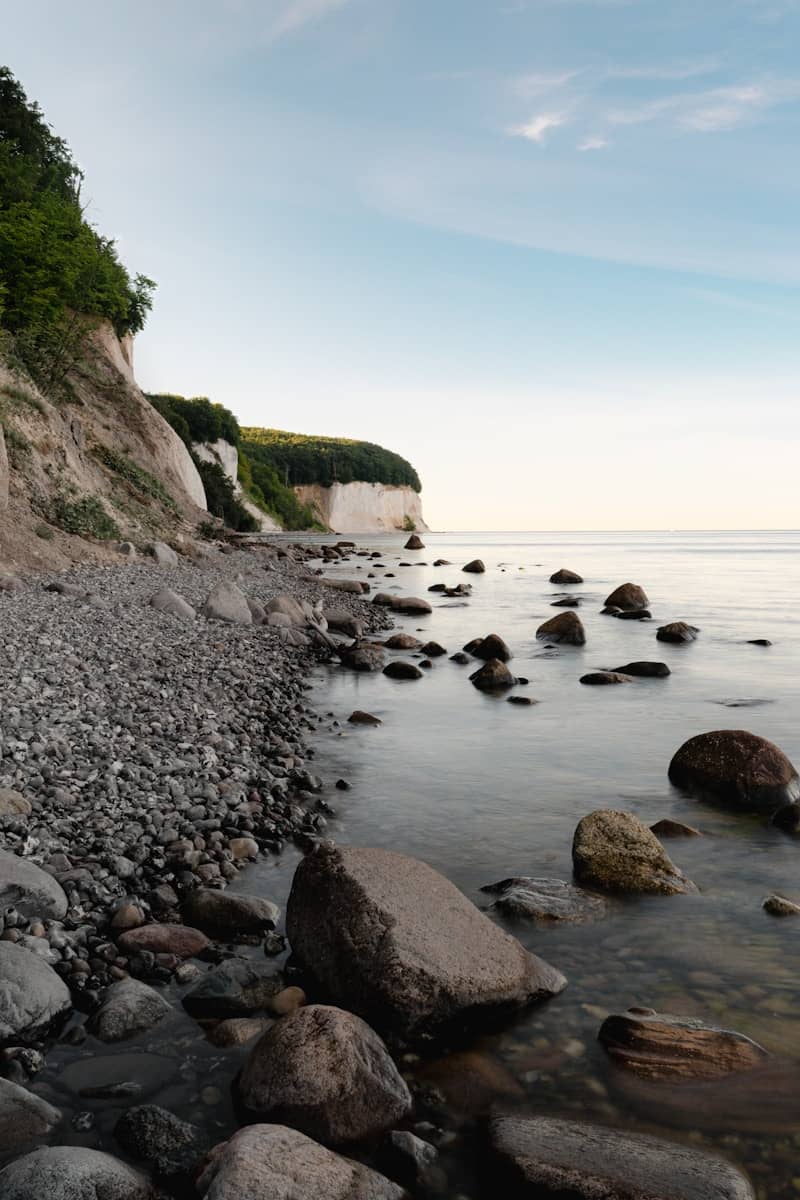 White chalk cliffs overlook a rocky beach and calm sea.