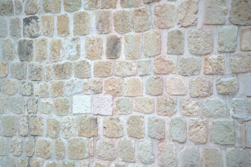 A wall constructed from rough rectangular beige and grey stones with light mortar