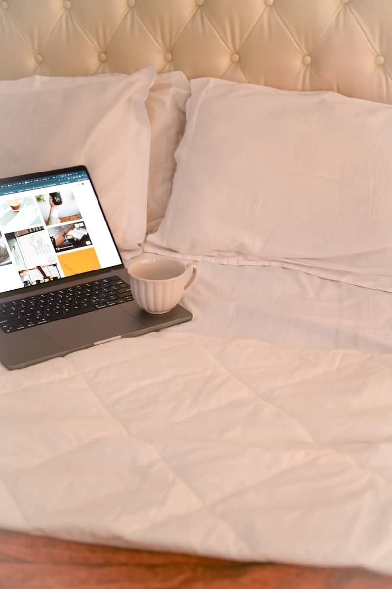 Laptop and coffee on a cozy, white bed.