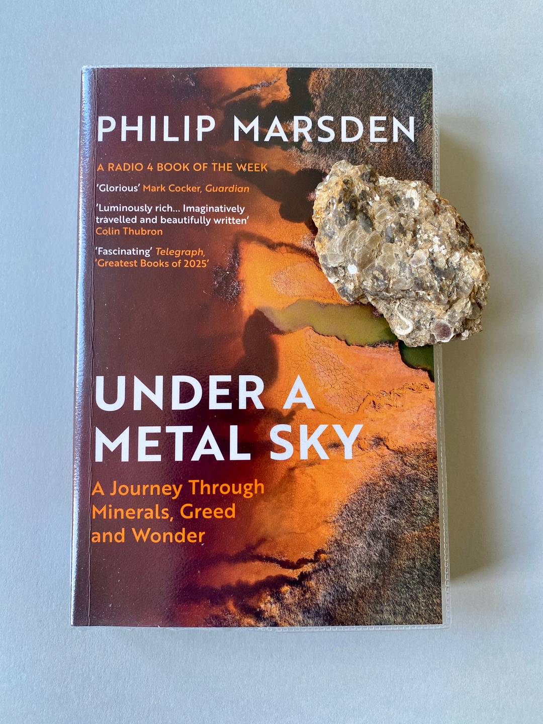 The front cover of a paperback book with a stone on top.