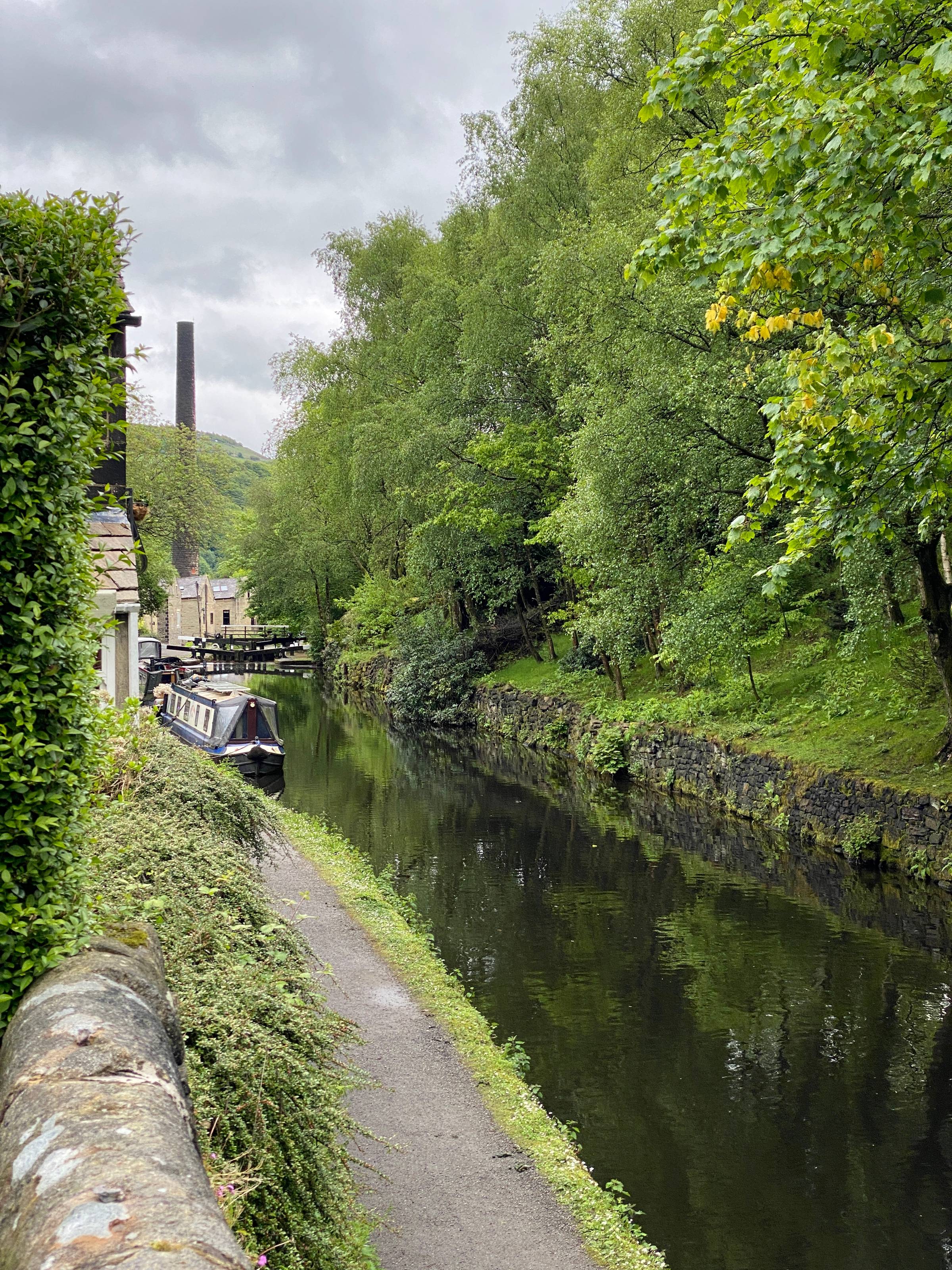 A leafy green canal with narrow boats and a mill chimney