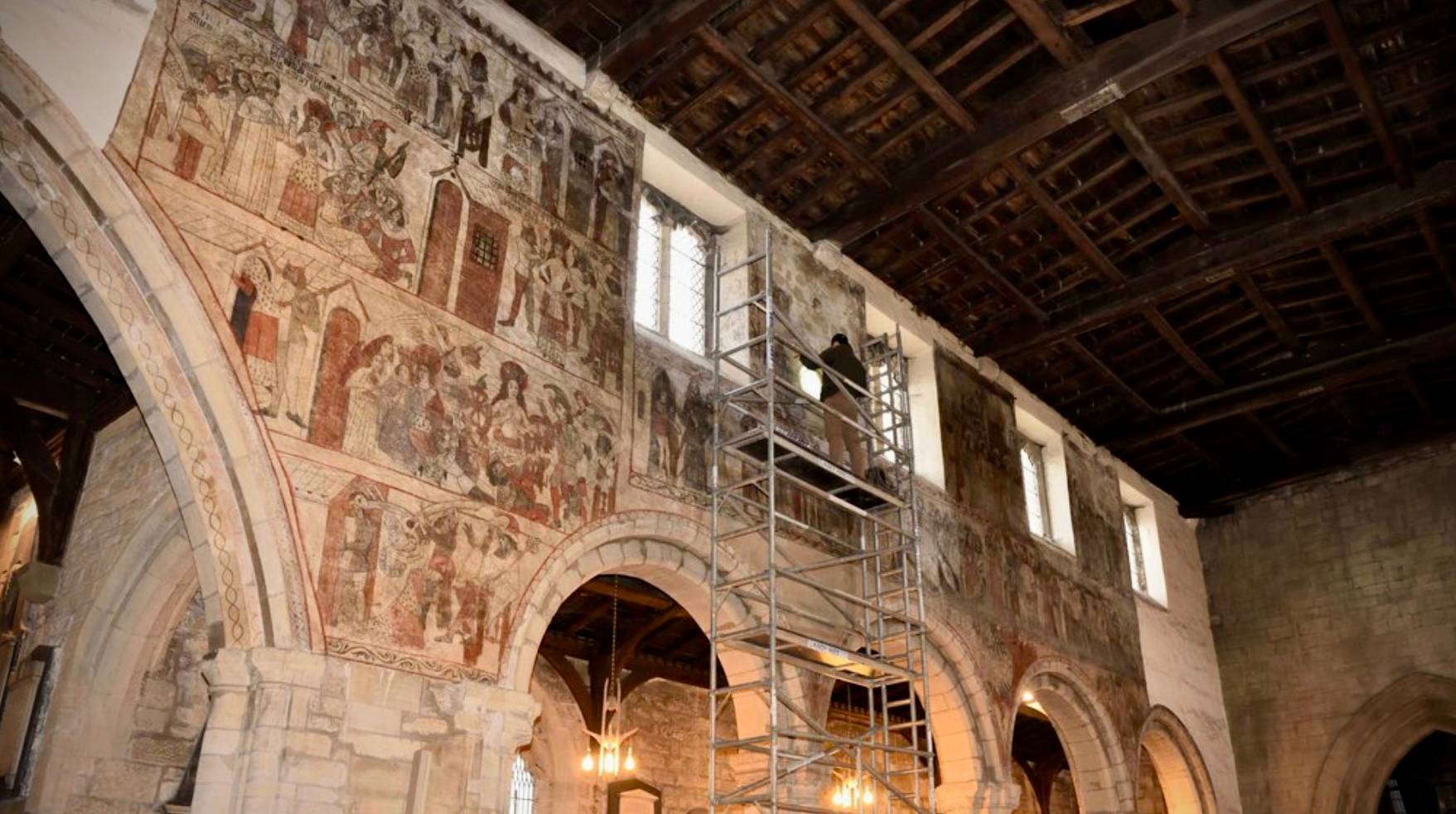 wall paintings in medieval church being restored using scaffolding tower.