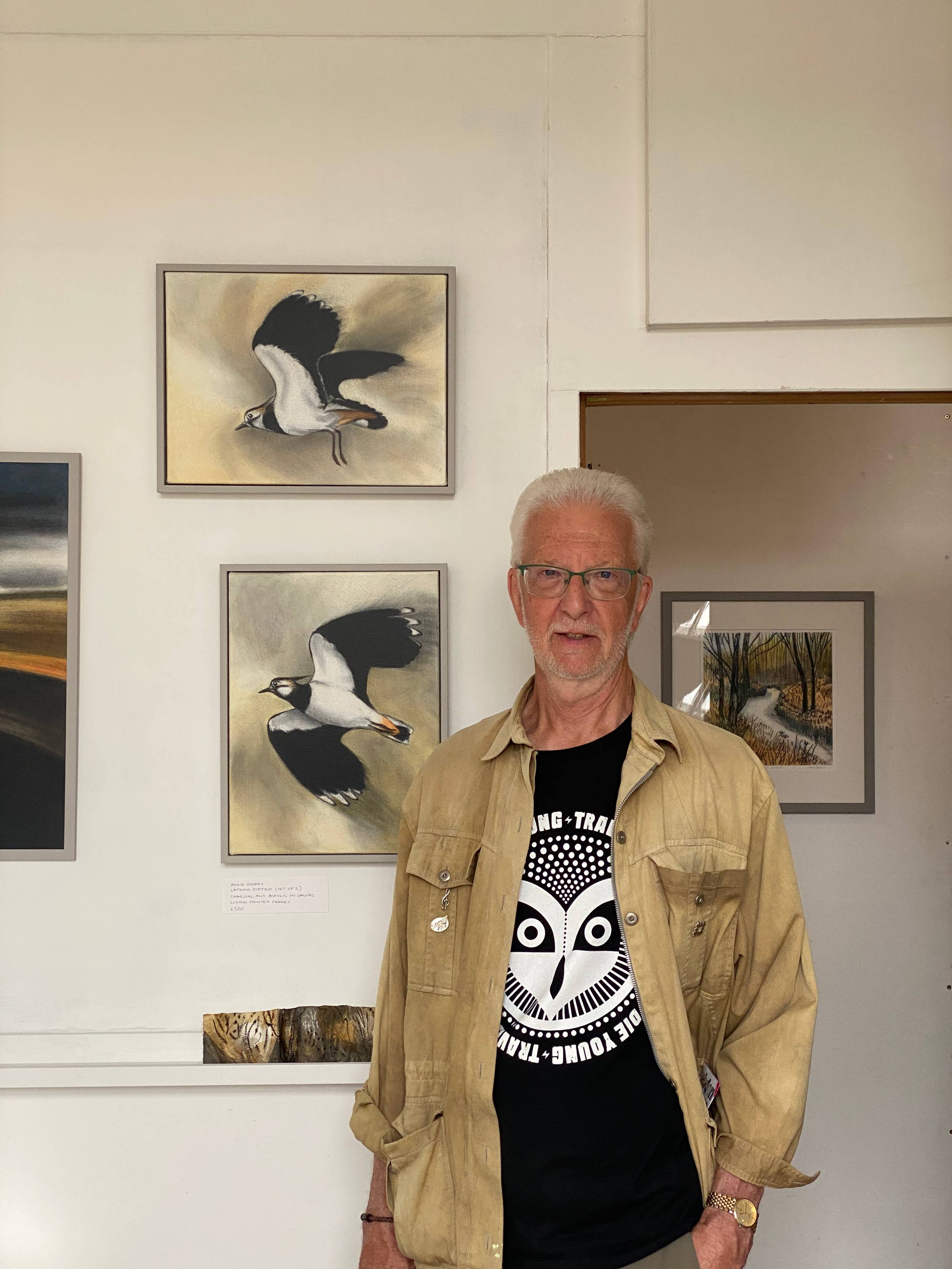 a man standing infront of bird paintings in a gallery.
