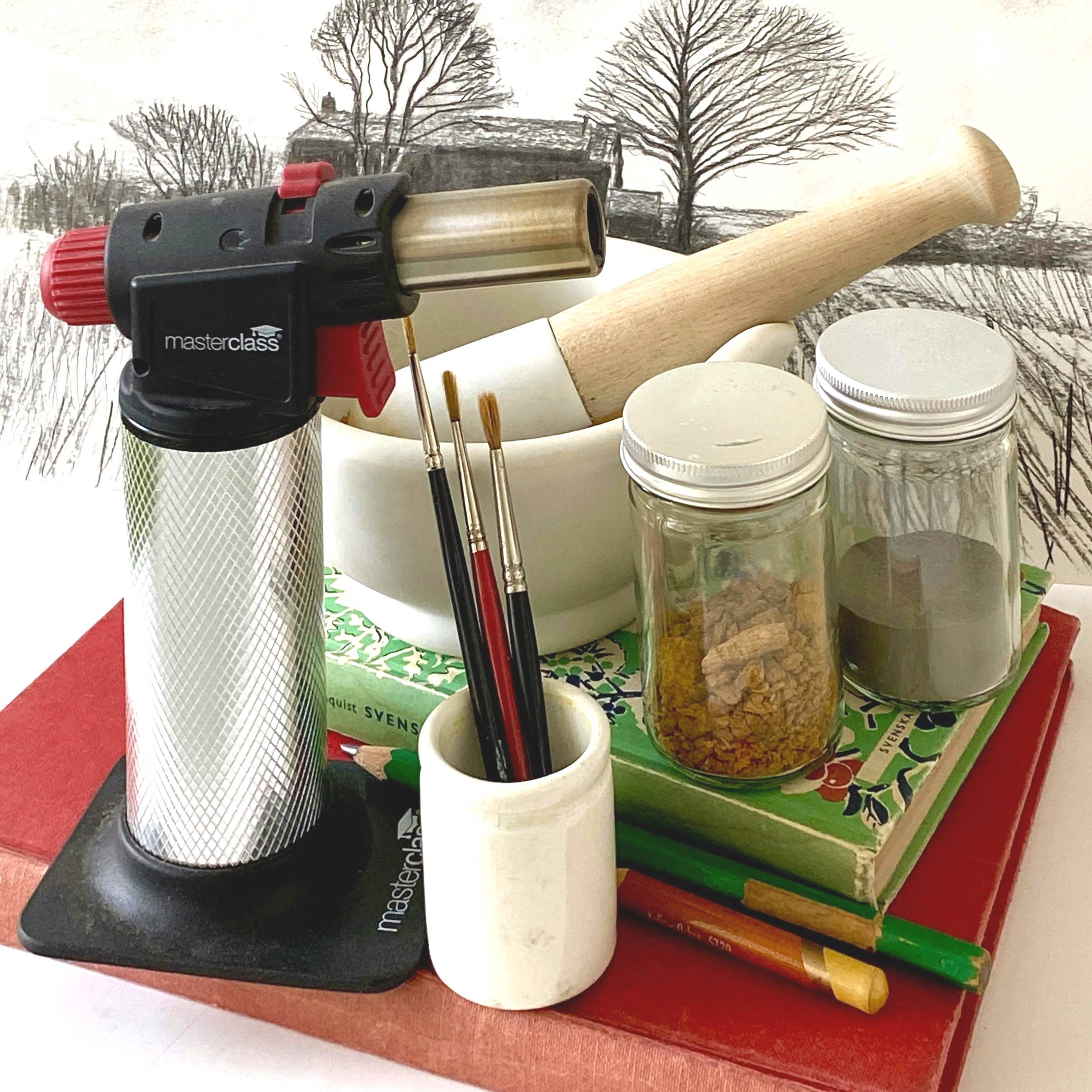 A blowtorch alongside artist's tools and materials.