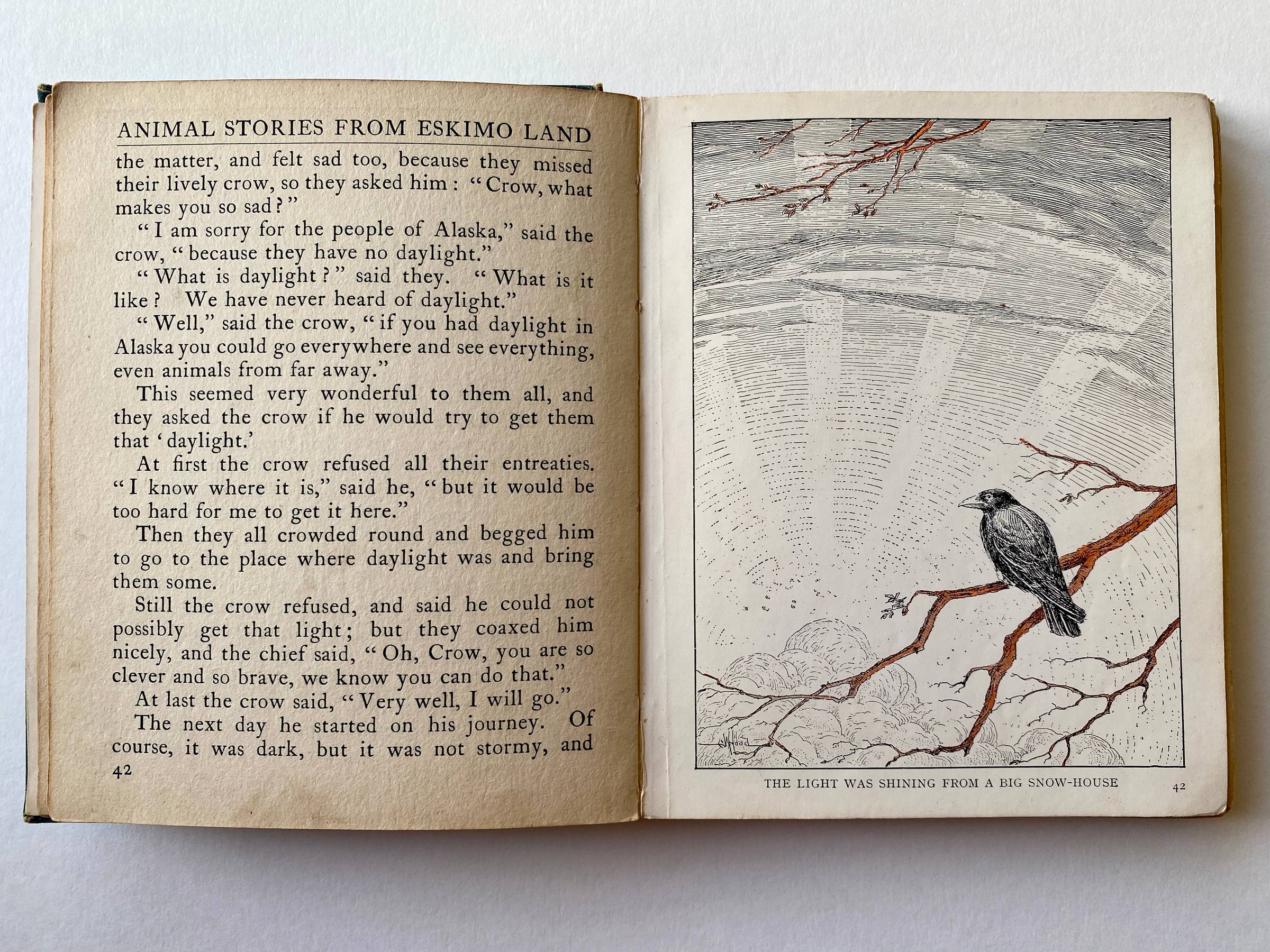 Old book with aged paper and illustration of a crow on branches with sun beams from an igloo.