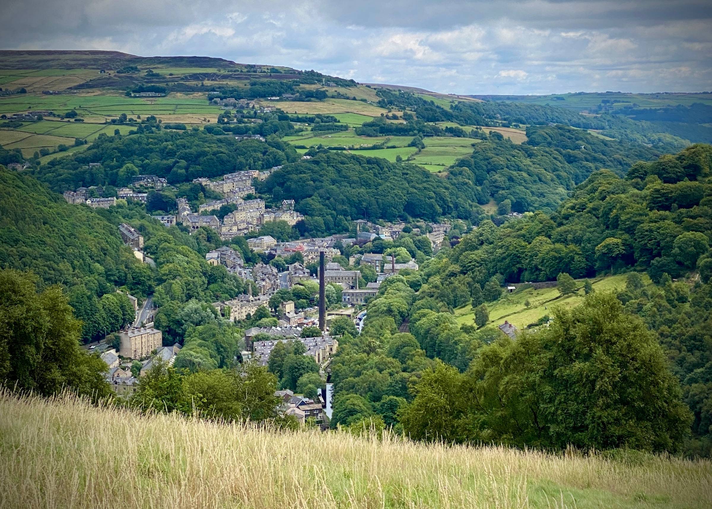 A distant view of Hebden Bridge from high up in a field. Big dark mill chimney.