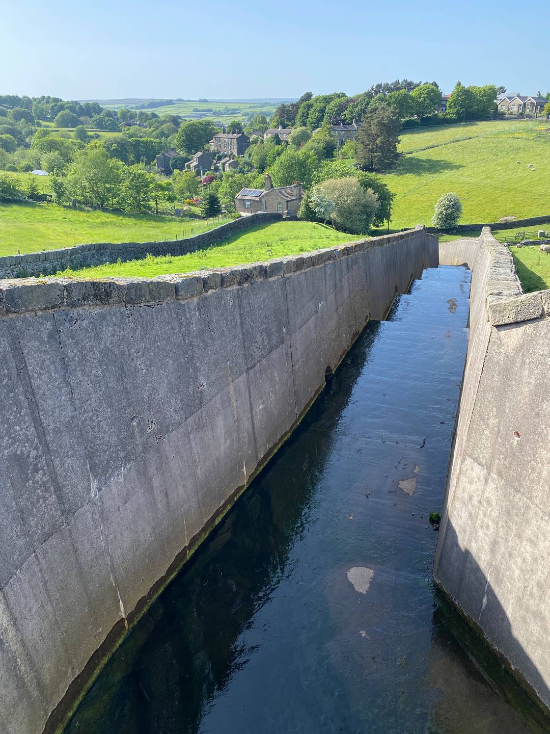 A concrete outflow from a reservoir in summer, green fields, blue sky