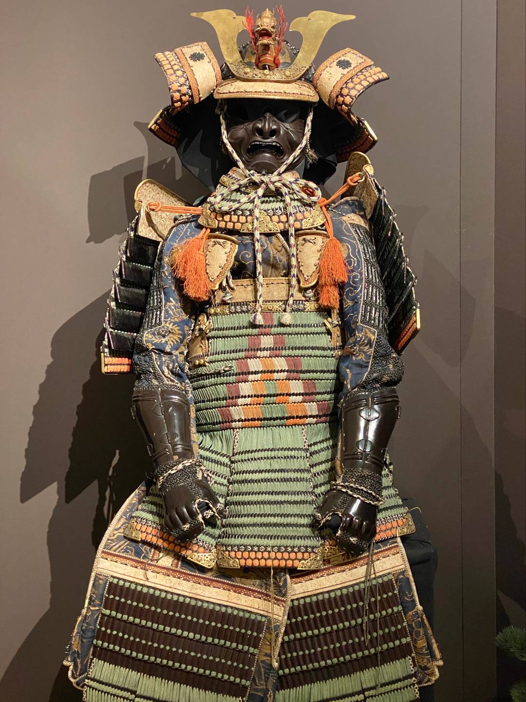 A suit of Japanese armour with green, orange and gold detail.