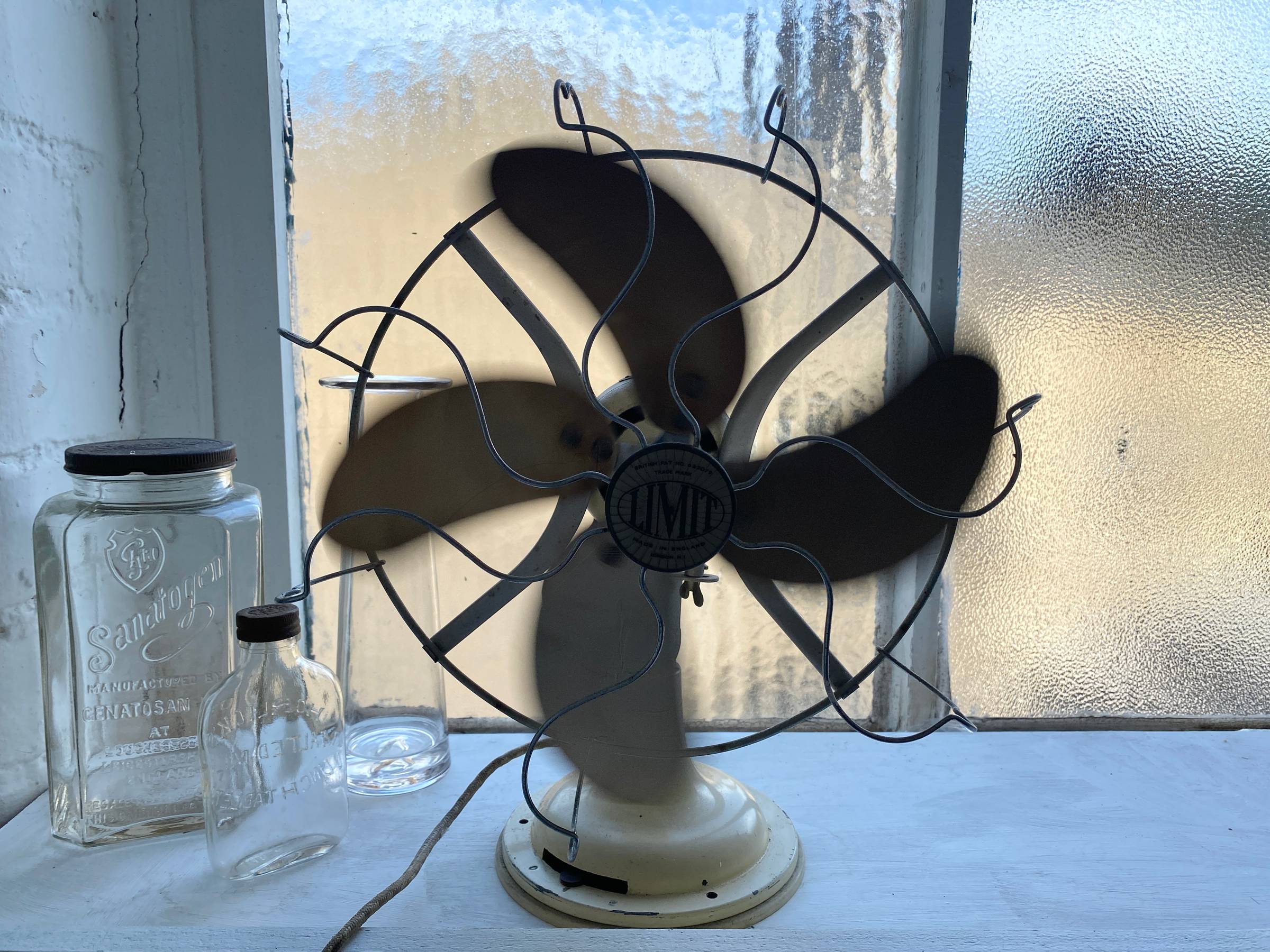 Silhouette of old mechanical fan on a windowsill with pale yellow behind.