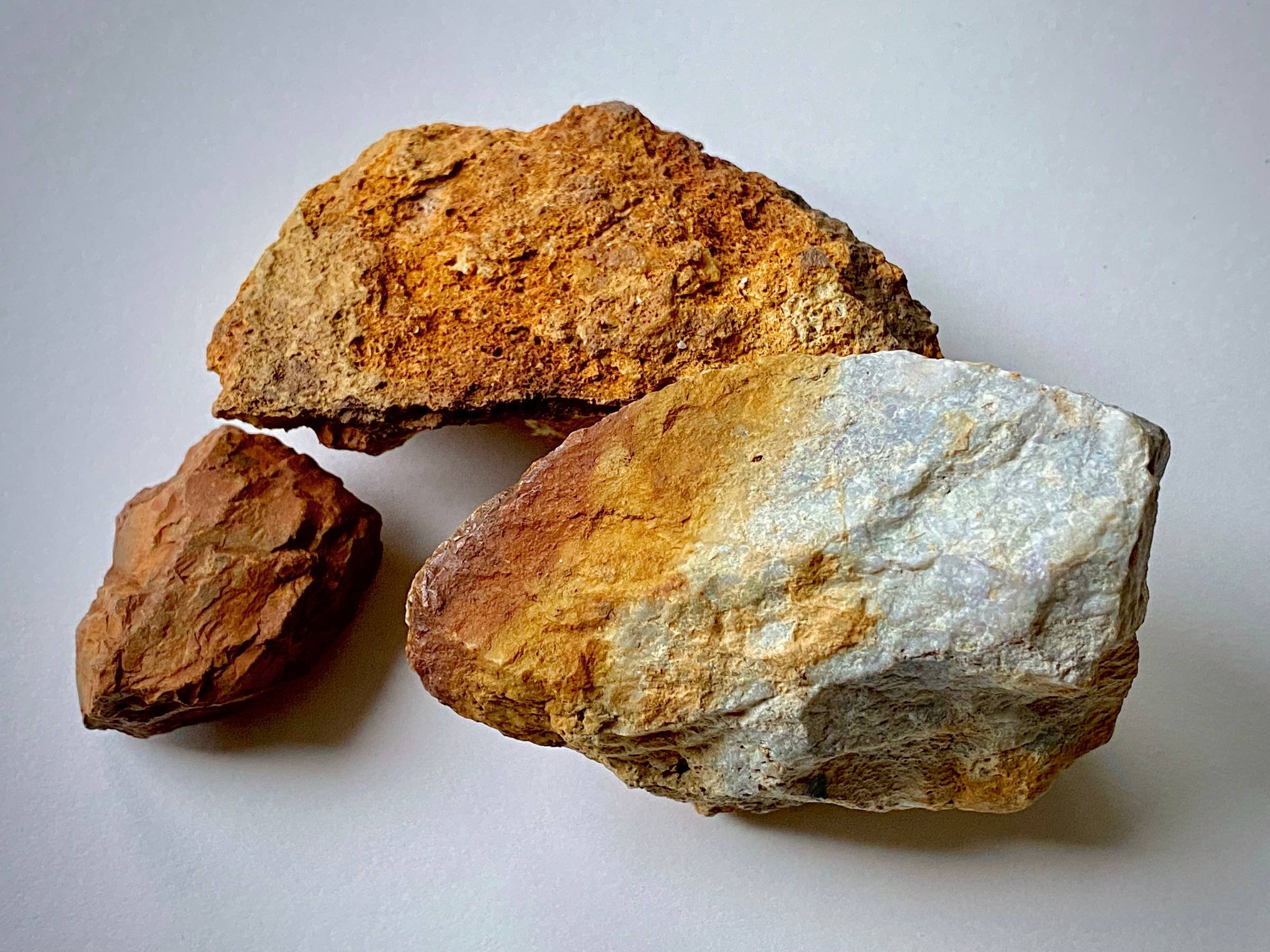 Three small pieces of stone, red, orangey yellow and white, all on a pale grey backgound.