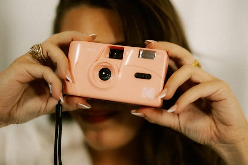 Woman holds a pink camera and looks through it.