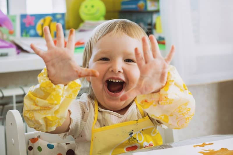 Happy child shows off colorful, messy hands.