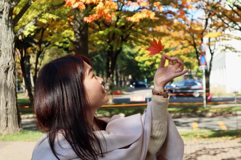 A woman holding a red leaf in a park