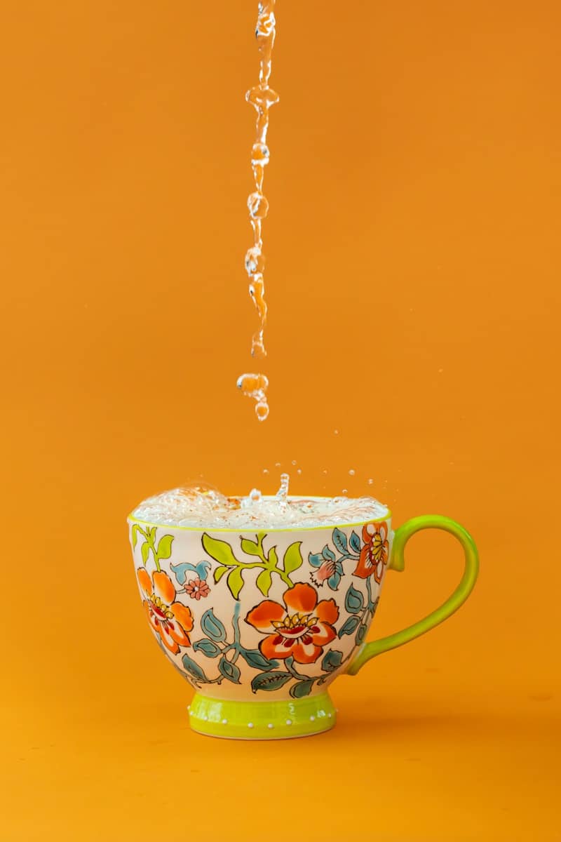 Water splashes into a colorful floral teacup.
