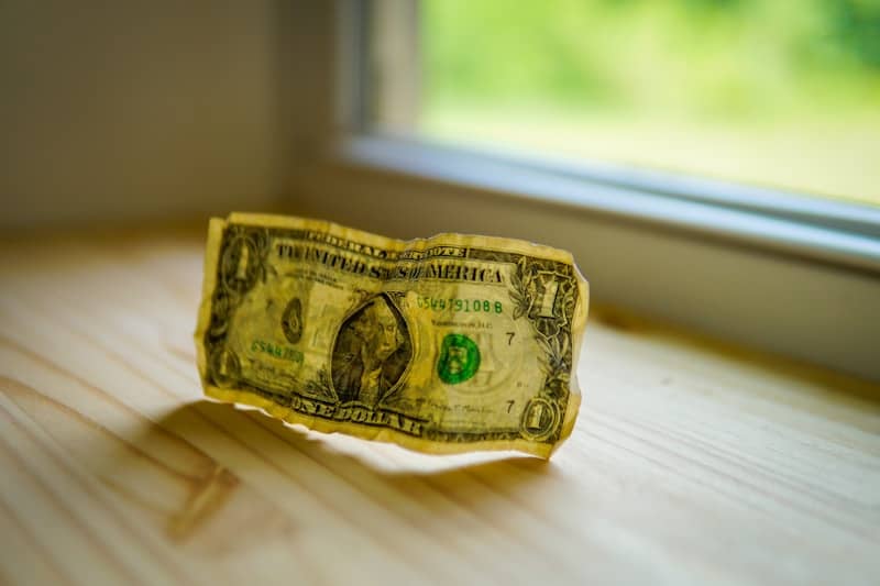 A crumpled dollar bill on a wooden surface.
