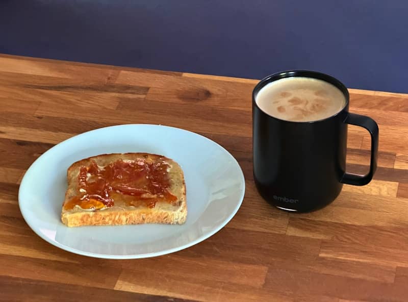 Toast with jam and a black coffee mug on wood.