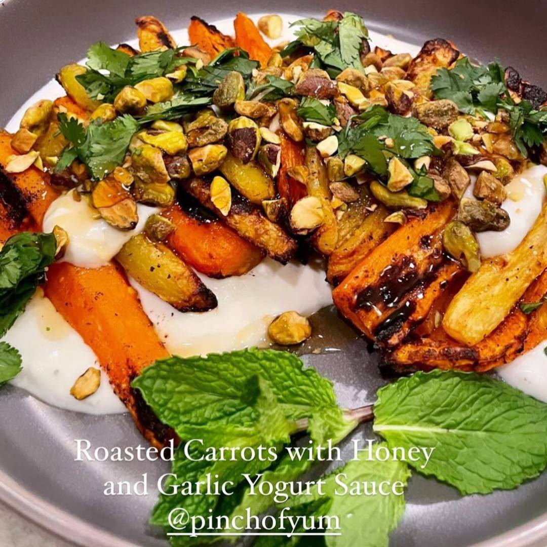 Roasted carrots on a bed of yogurt with nuts and herbs on top.