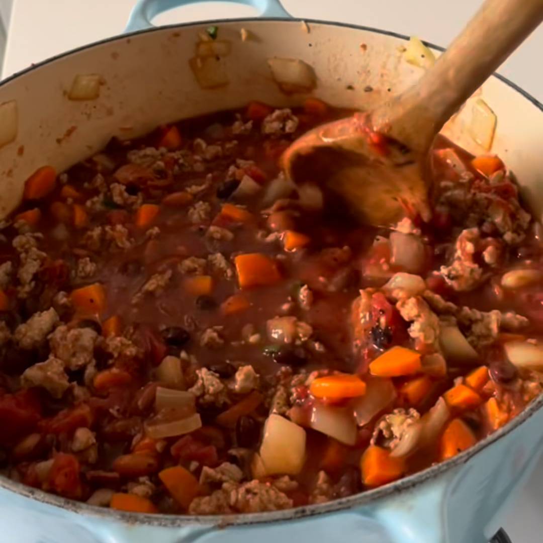 Person stirring chili with a wooden spoon