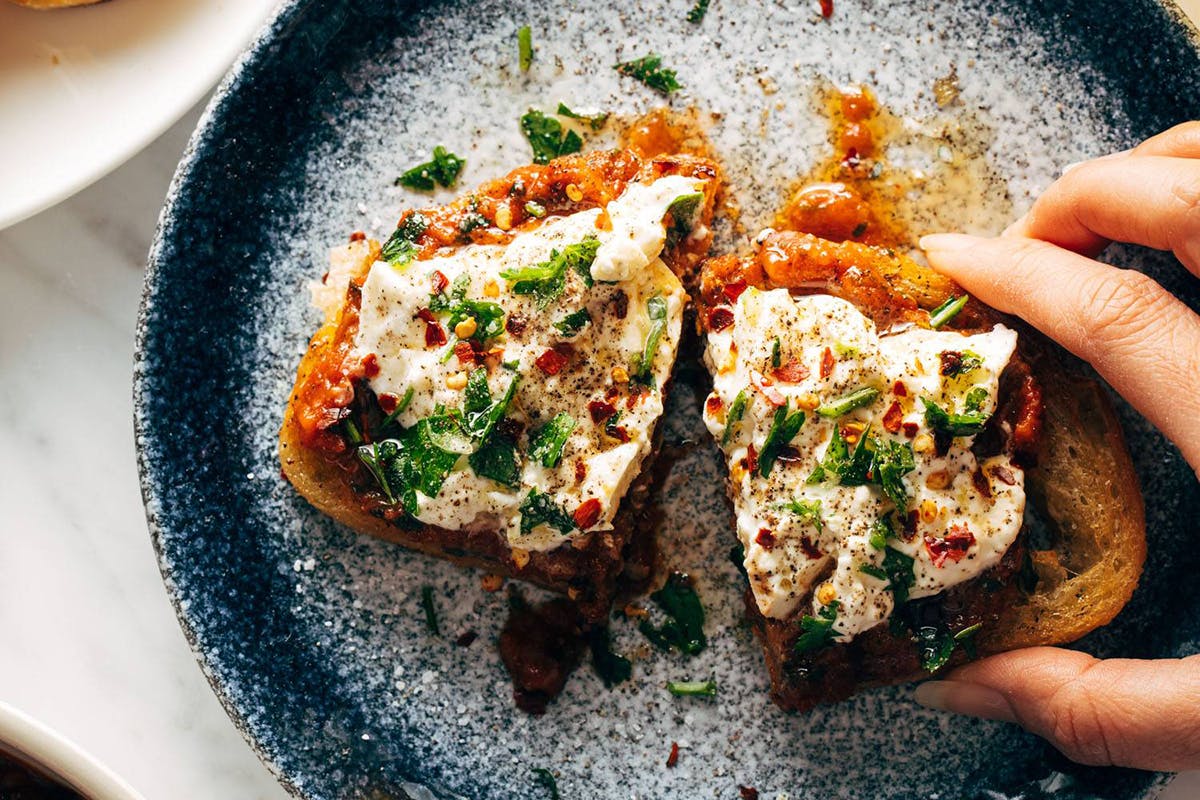 White hand grabbing zaalouk toast on a plate