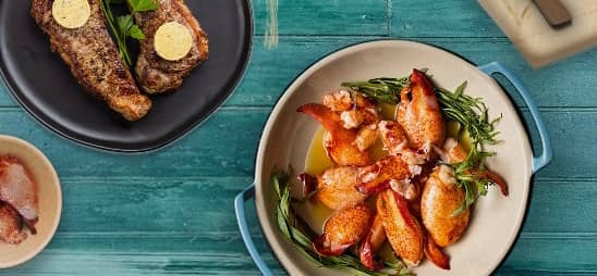 Lobster and steak on plates on a blue background.