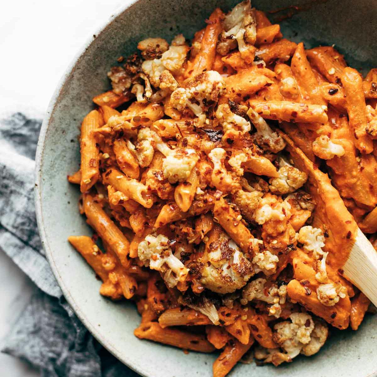 Red Pepper Cashew Pasta with Roasted Cauliflower in a bowl in a wooden spoon