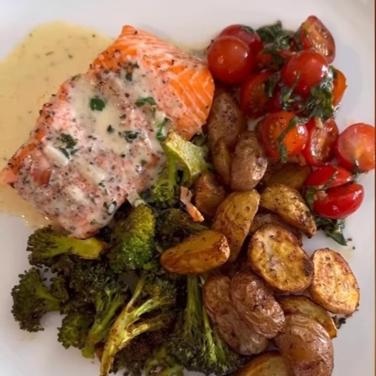 Salmon on a plate with tomatoes, lemon sauce, broccoli, and potatoes