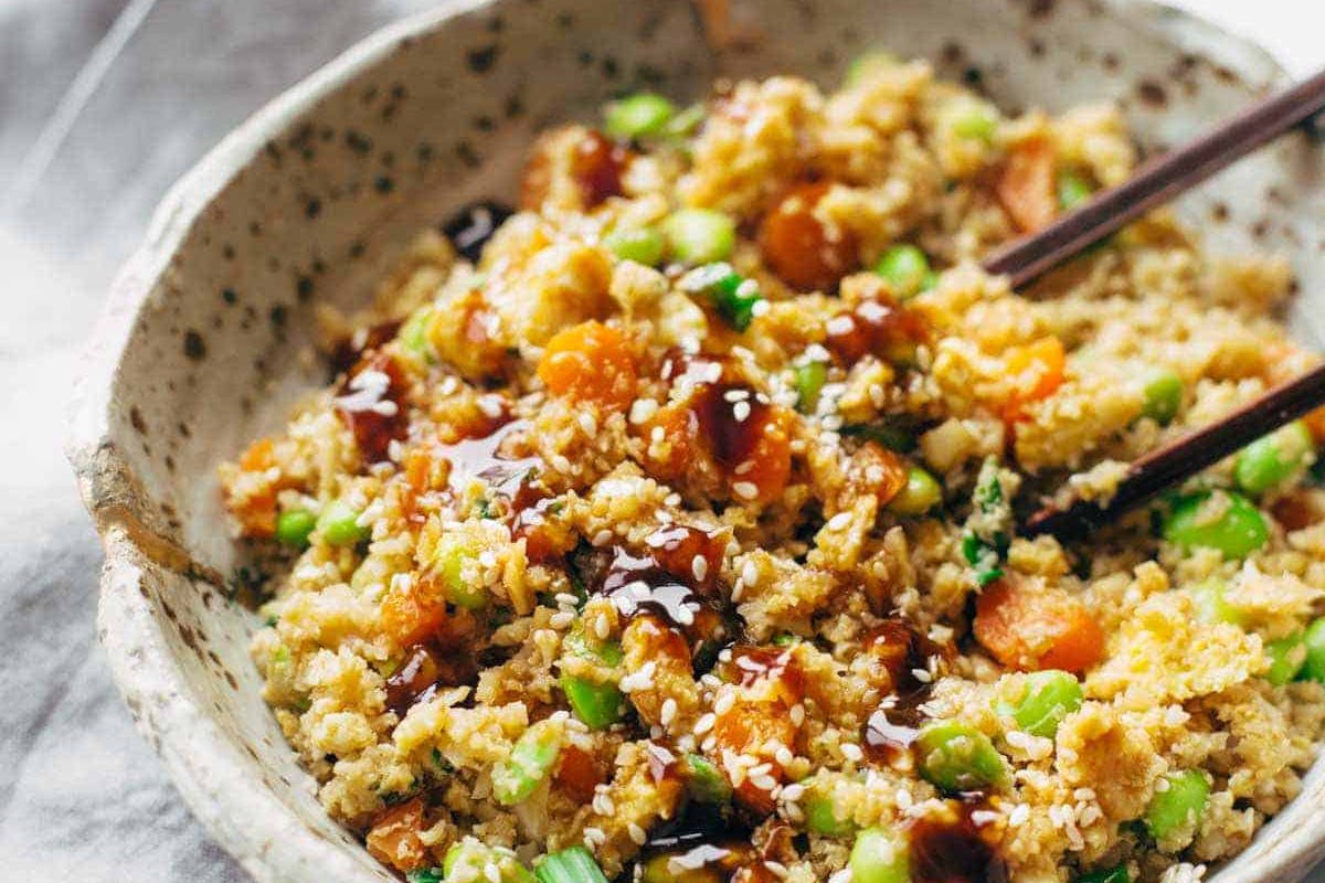 Cauliflower fried rice topped with soy sauce in a bowl with chopsticks