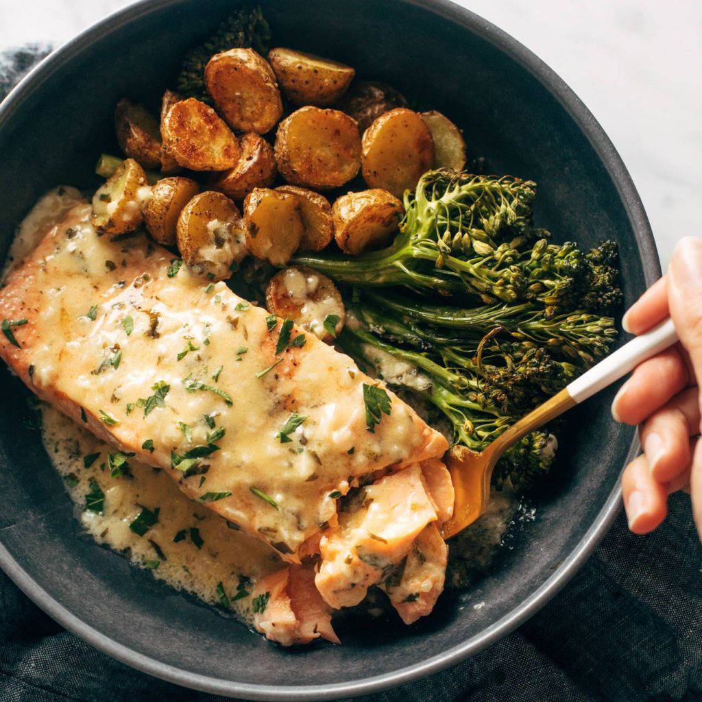 Baked salmon in a bowl with potatoes, broccolini, and lemon sauce.