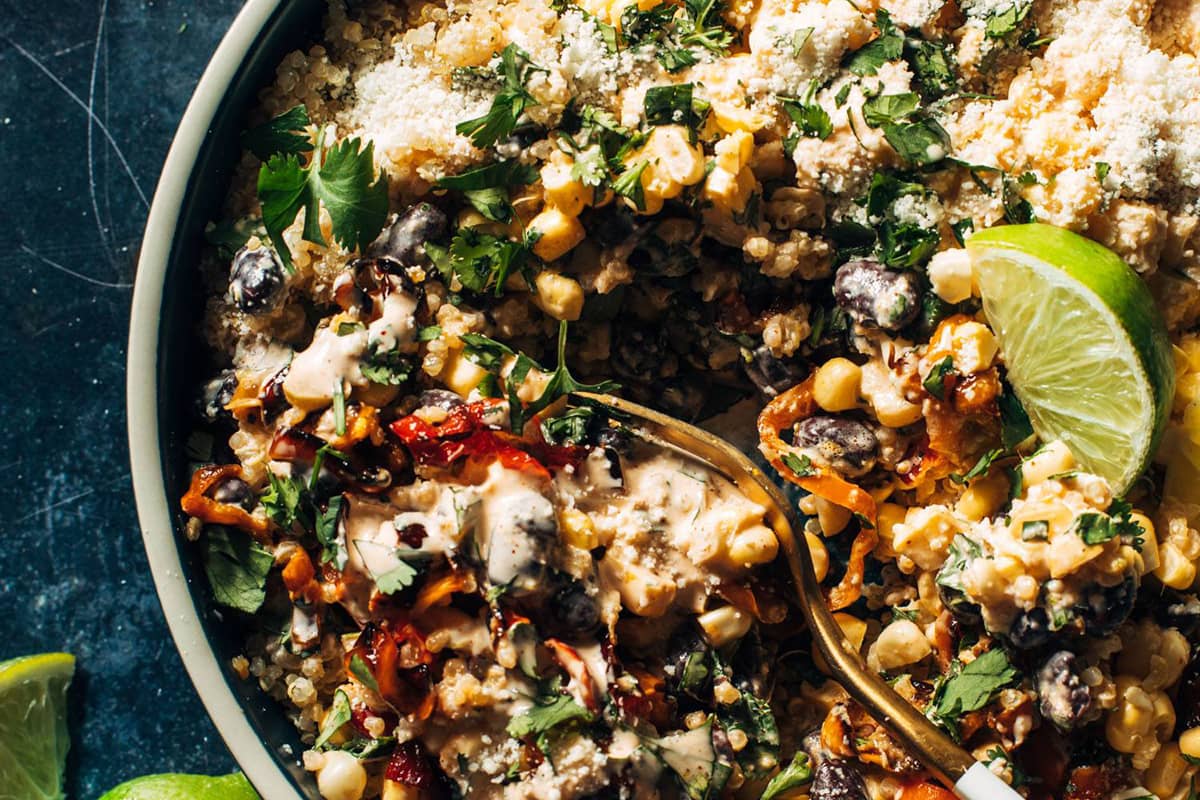 Elote style salad in a bowl with a lime and a fork