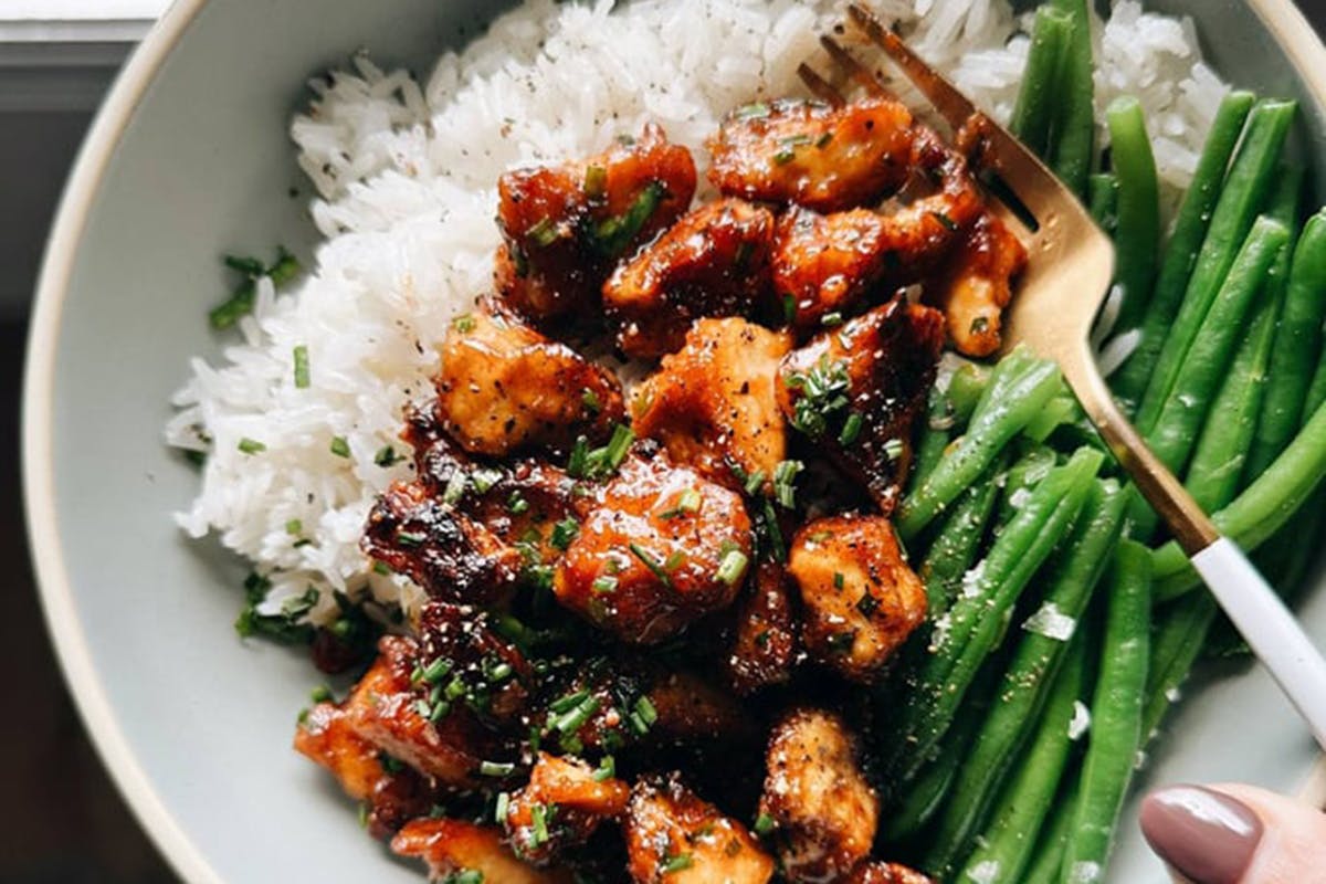 White hand holding a bowl of sesame apricot tofu with green beans and rice