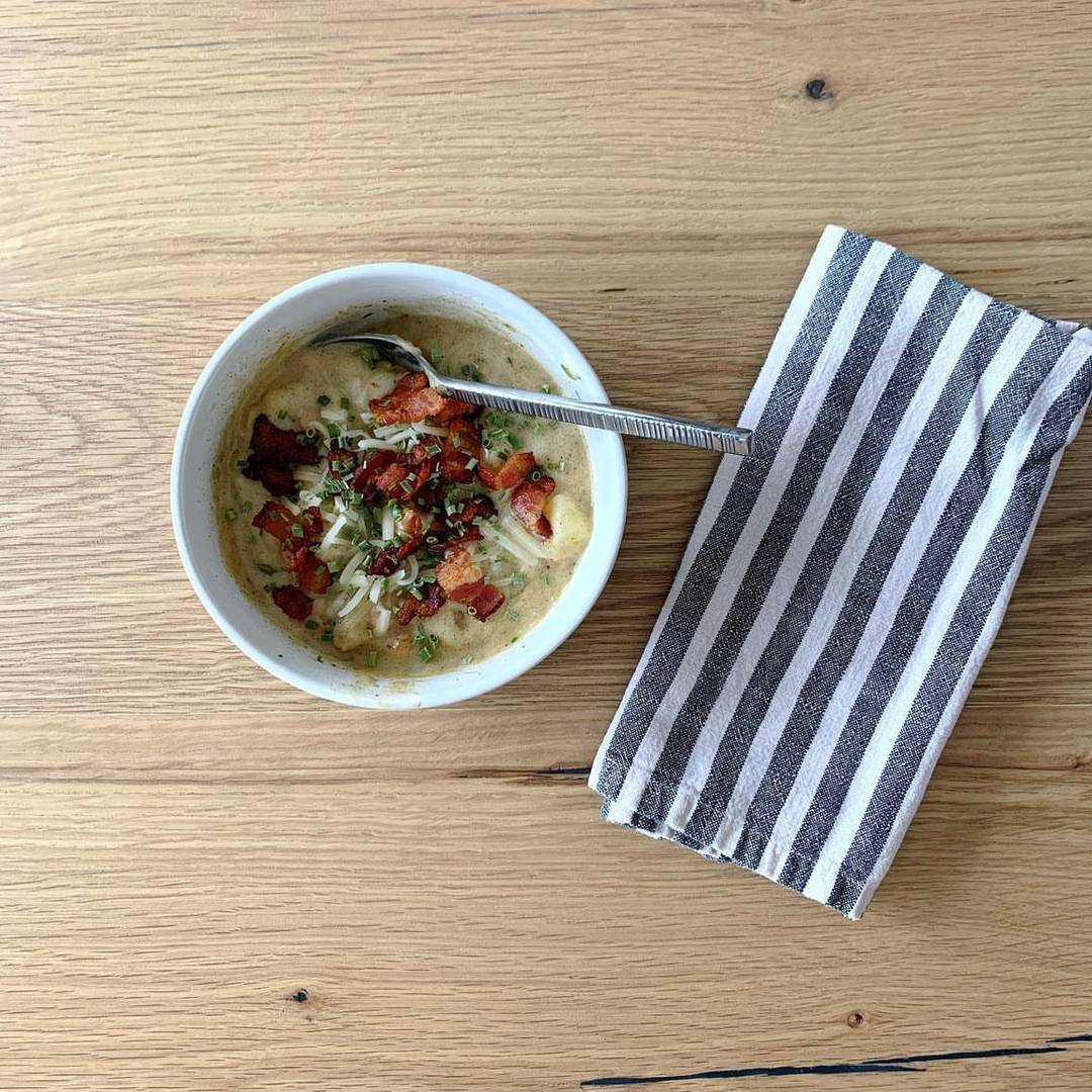 Potato soup topped with bacon in a bowl with a napkin on the side