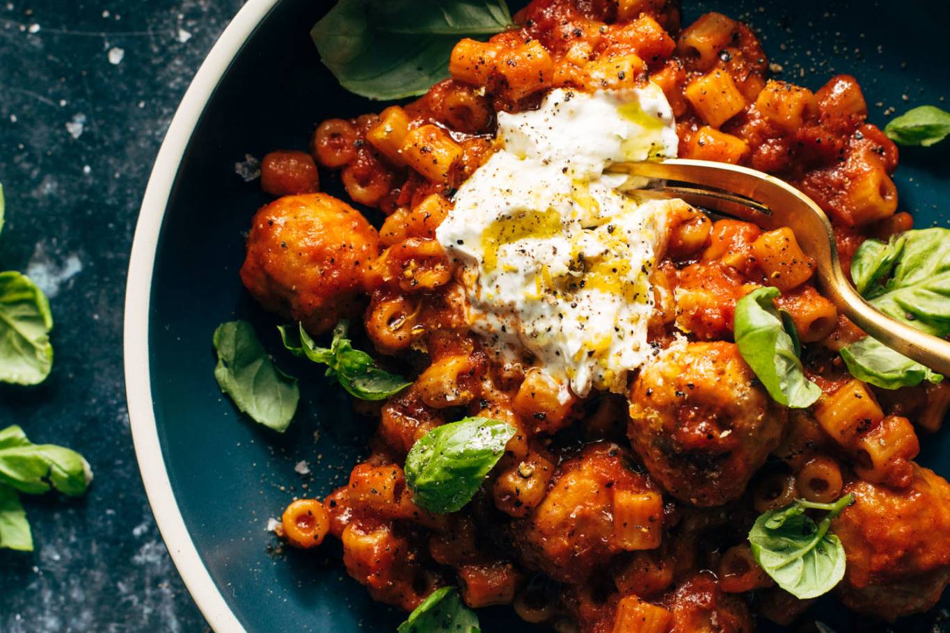 Pasta with meatballs in a bowl with ricotta and basil on top.
