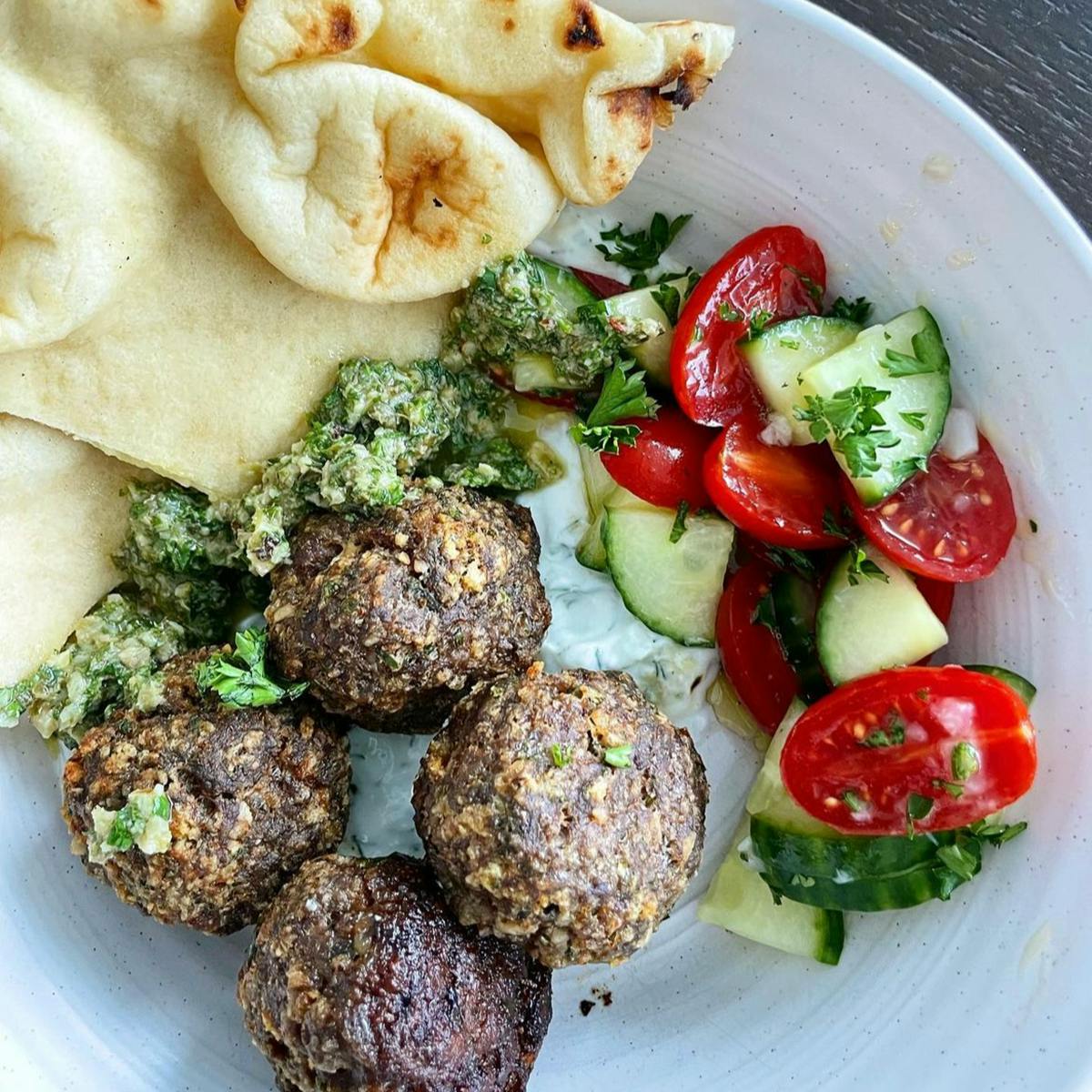 Meatballs and tomato salad with green sauce on a plate with bread