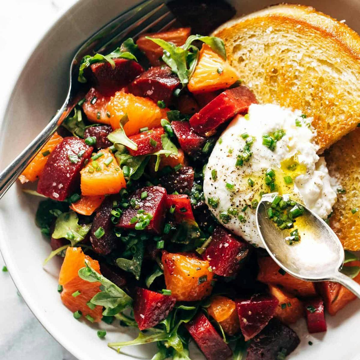 Beet and burrata salad in a bowl with a spoon and fried bread