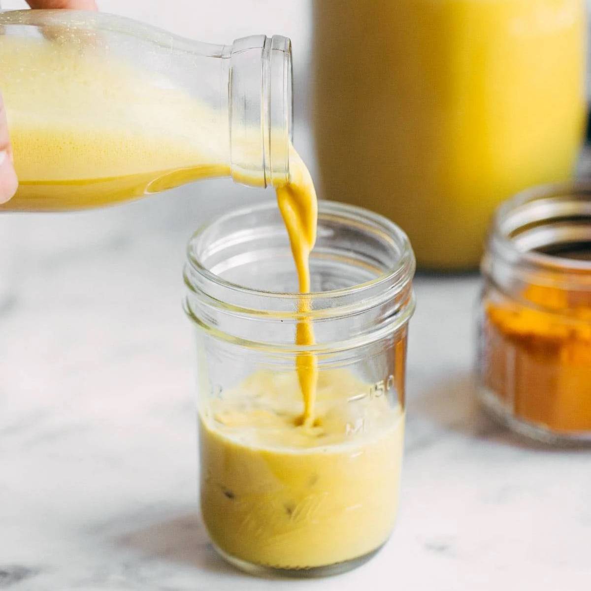 Hand pouring cashew golden milk latte into a jar