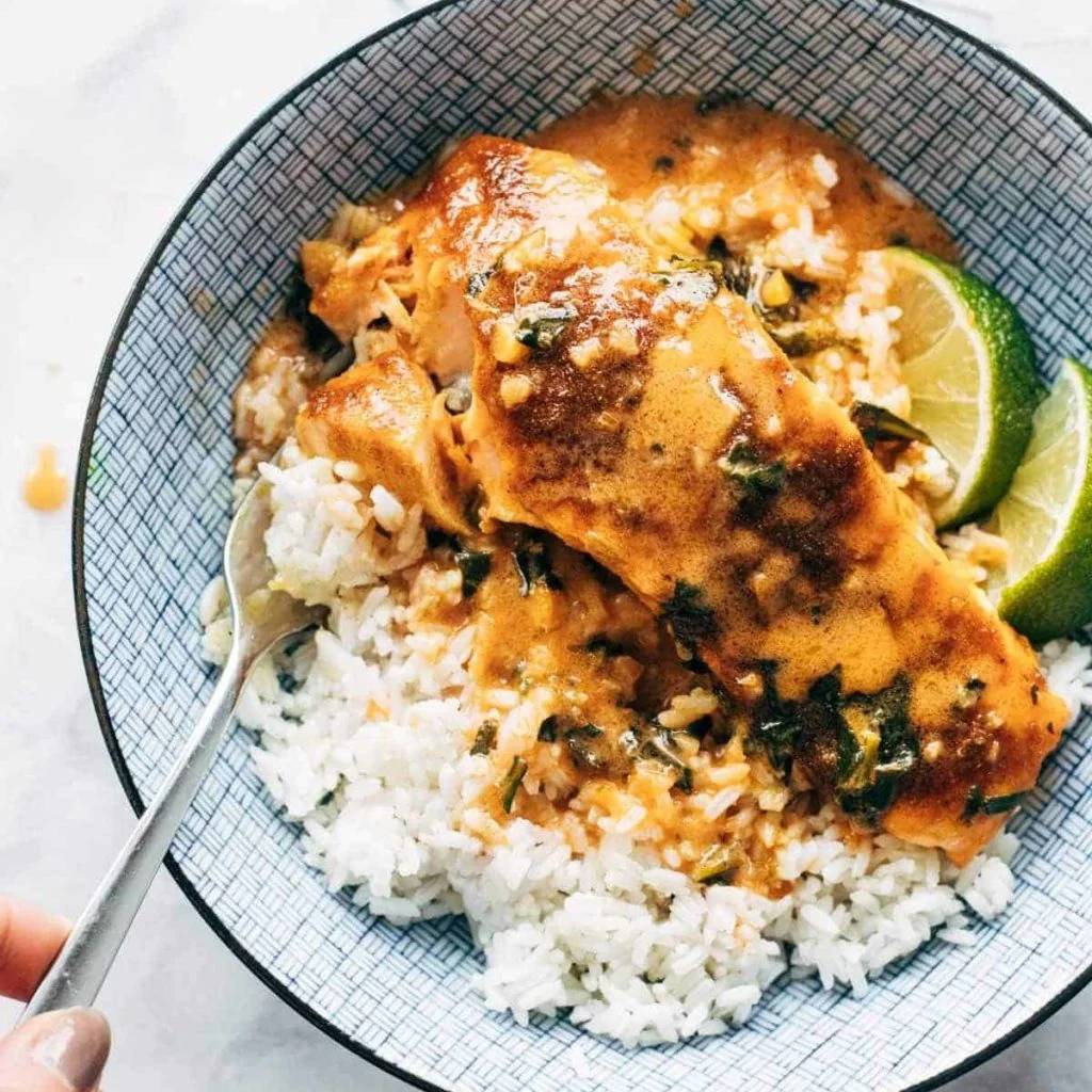 Coconut curry salmon in a bowl with rice and lime wedges.