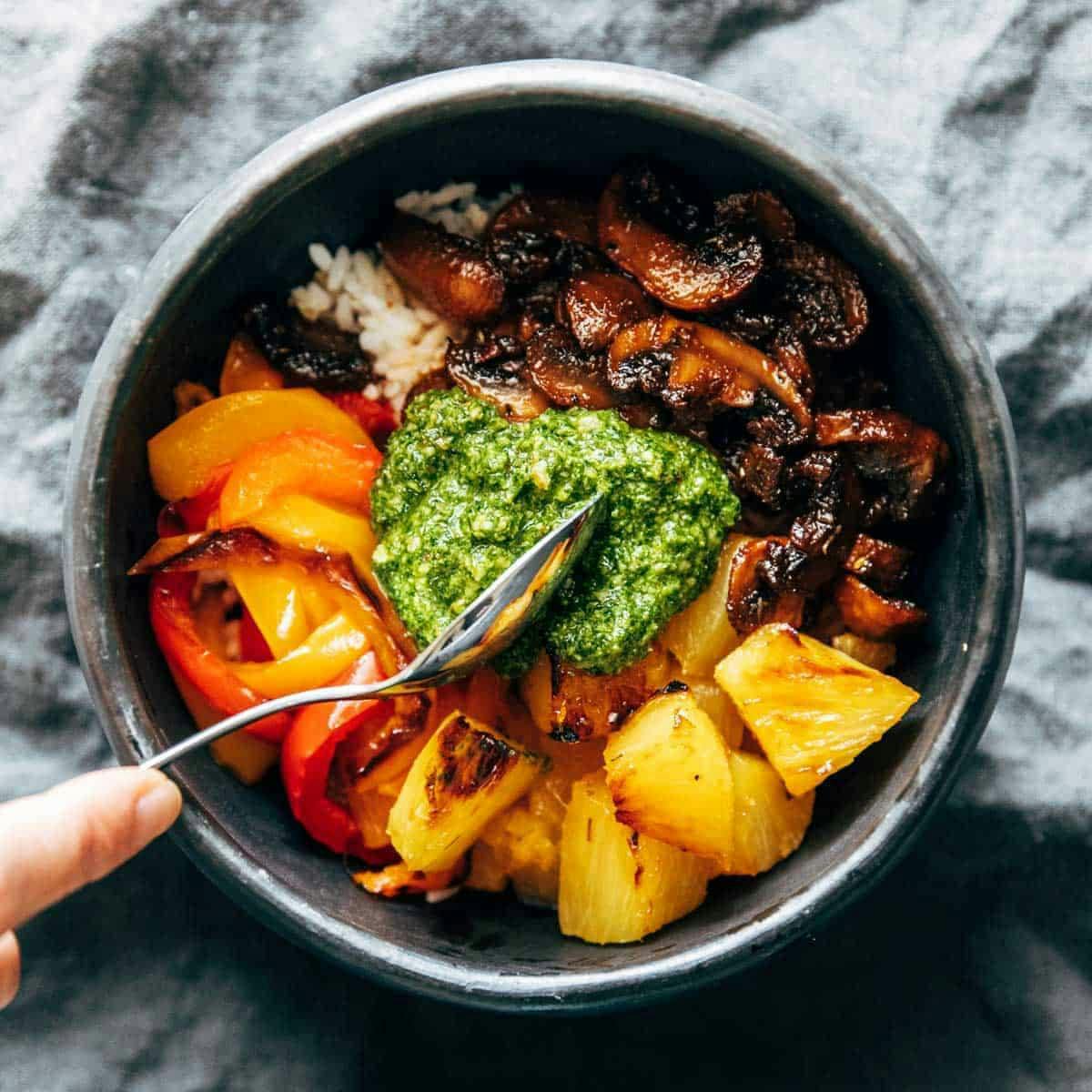 White hand holding a fork in a bowl of roasted mushrooms with toppings