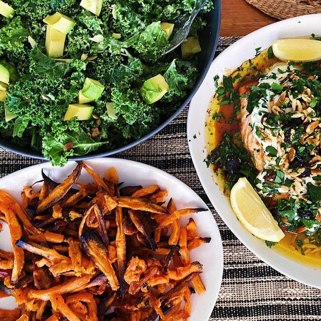 Avocado kale caesar salad with a plate of sweet potato fries