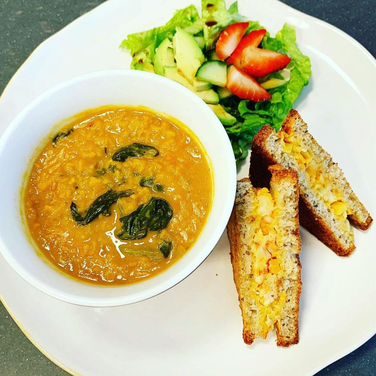Red lentil soup in a bowl on a plate with a sandwich and salad