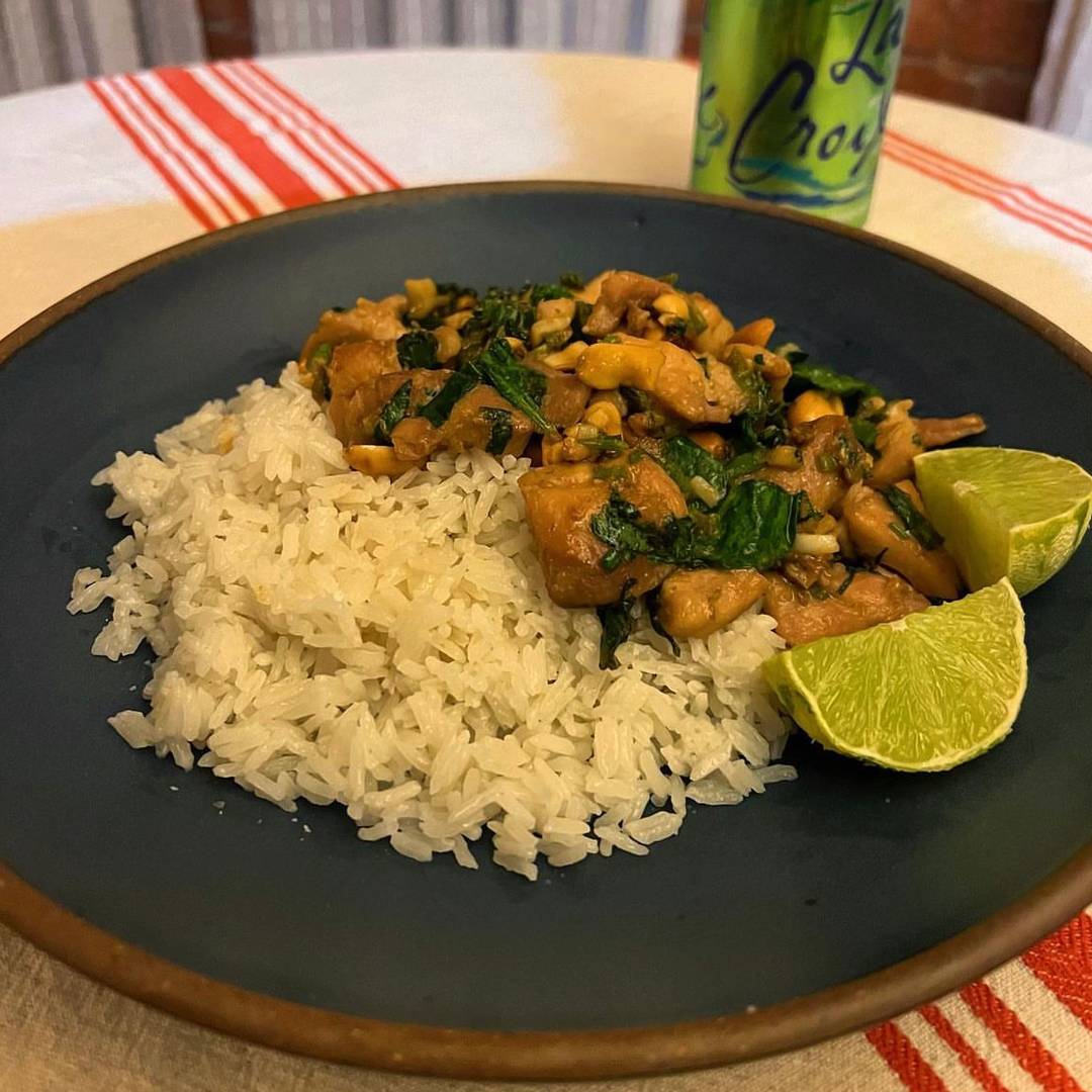 Ginger peanut chicken on a blue plate with rice and lime wedges