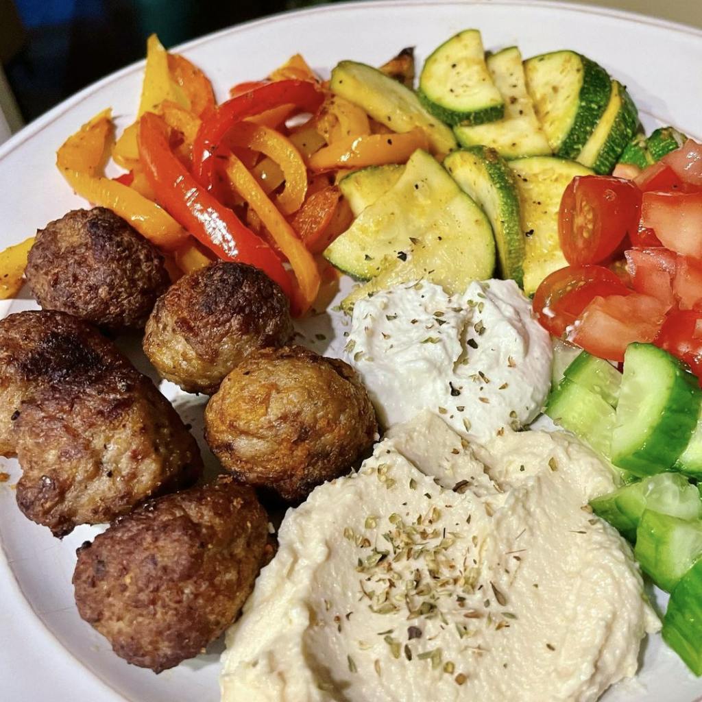 A plate with harissa meatballs, hummus, whipped feta, and veggies.