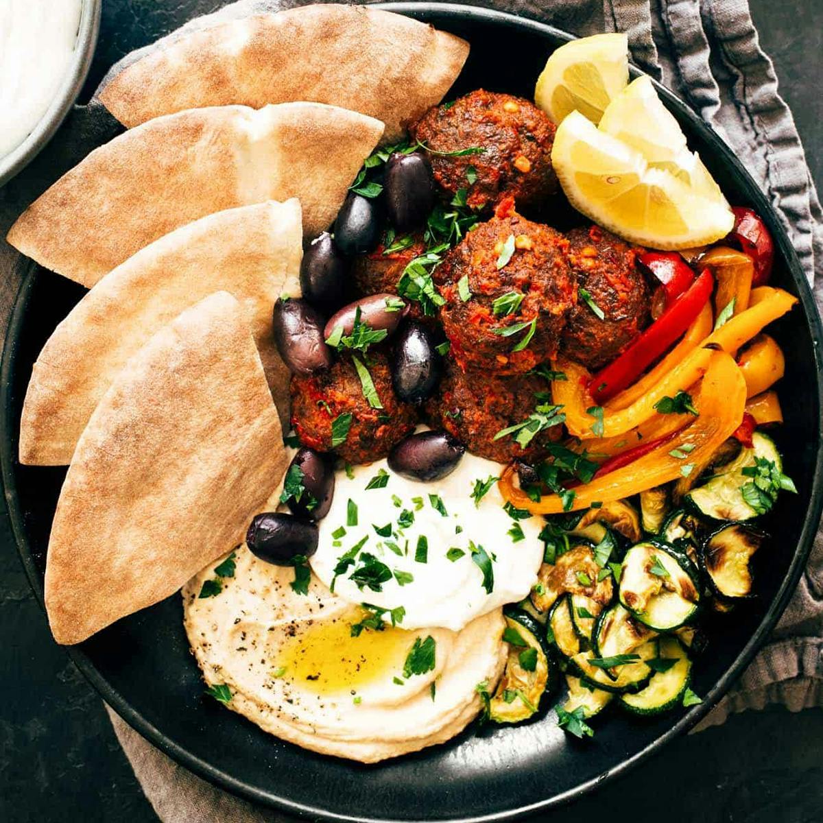 Meatballs in a bowl with feta, peppers, pita, olives, hummus, and zucchini