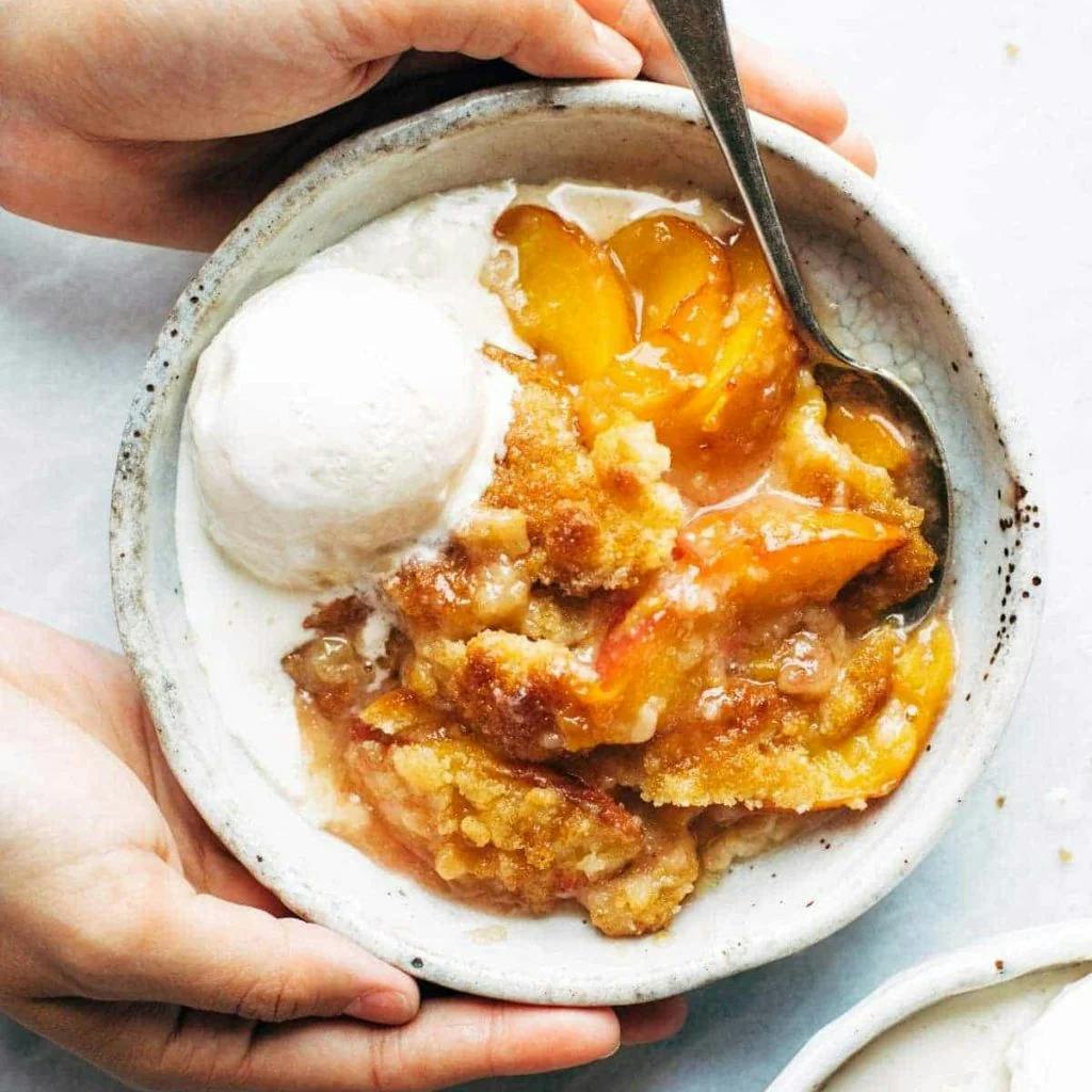 Peach cobbler in a bowl with a scoop of vanilla ice cream.