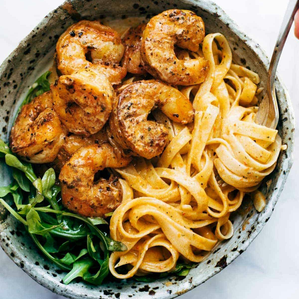 Red pepper fettuccine with shrimp and greens in a bowl with a fork