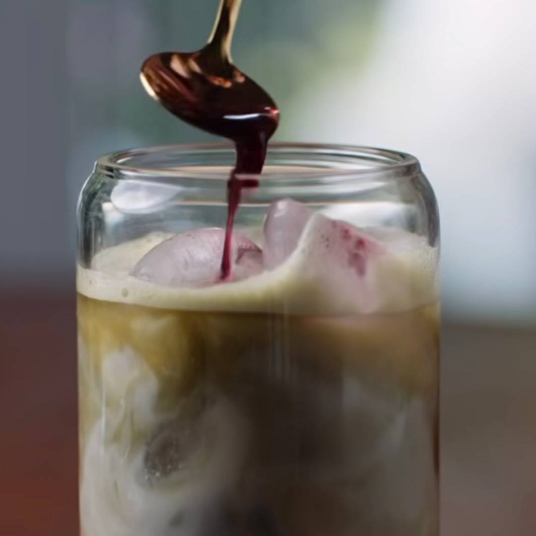 Blueberry syrup being poured into matcha latte