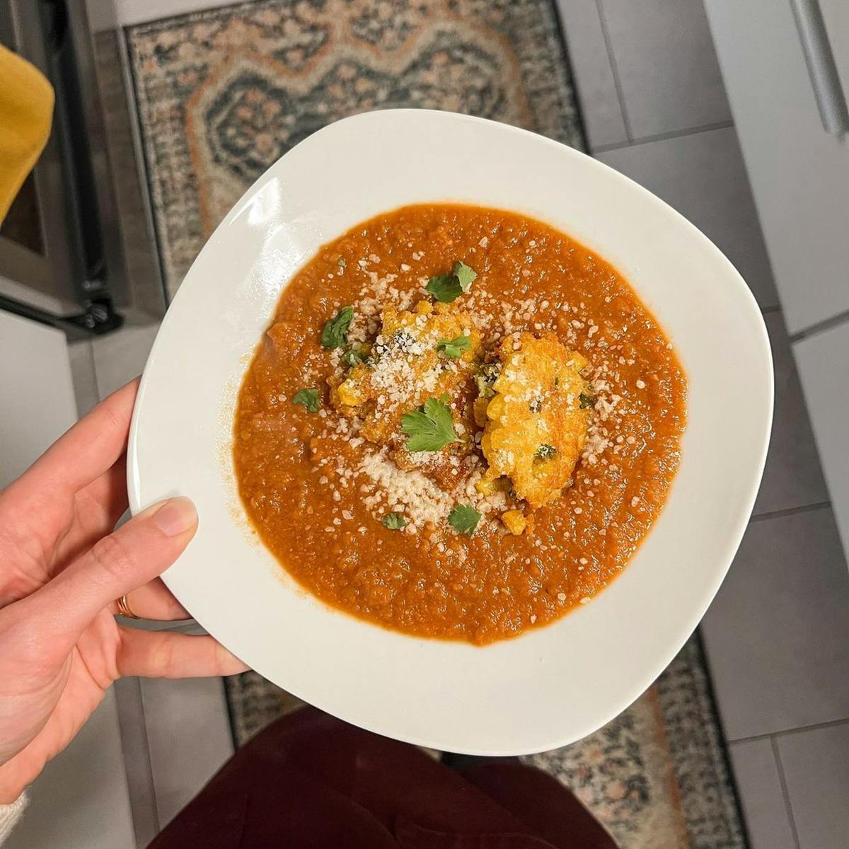 White hand holding a bowl of soup with corn fritters